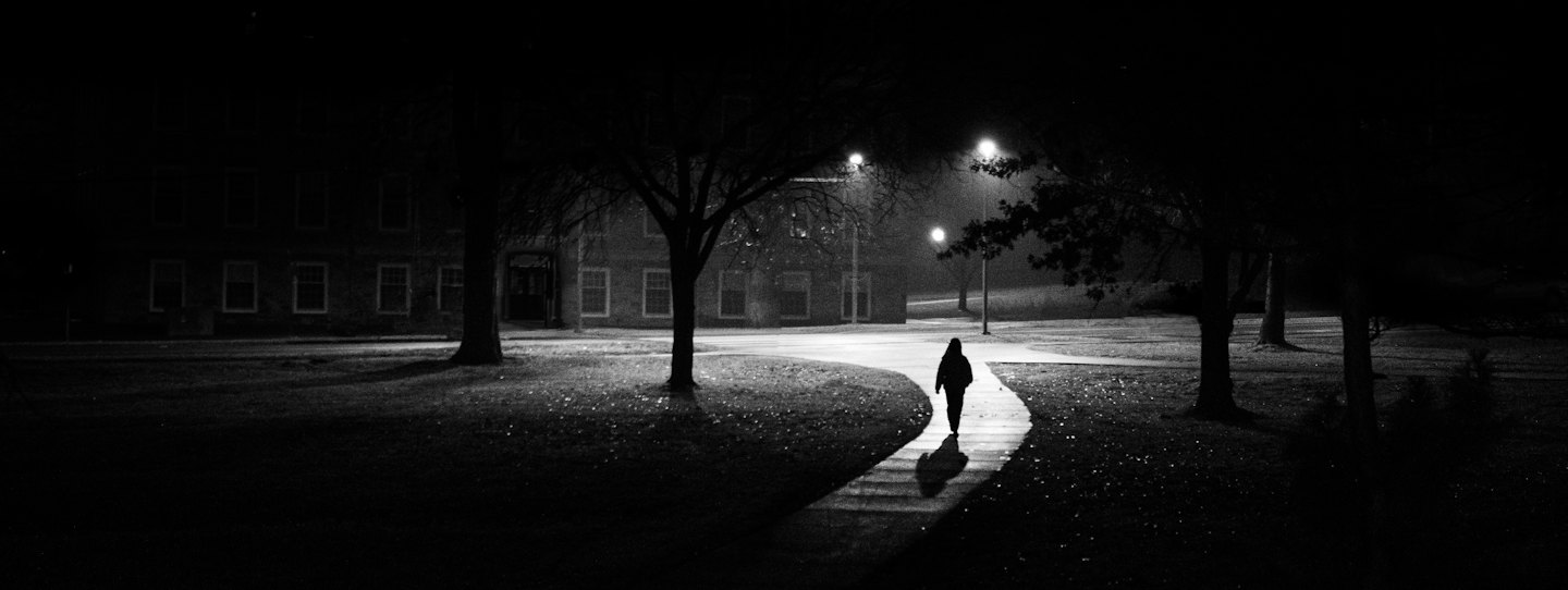 Silhouetted person walks away on a wet, winding path at night.