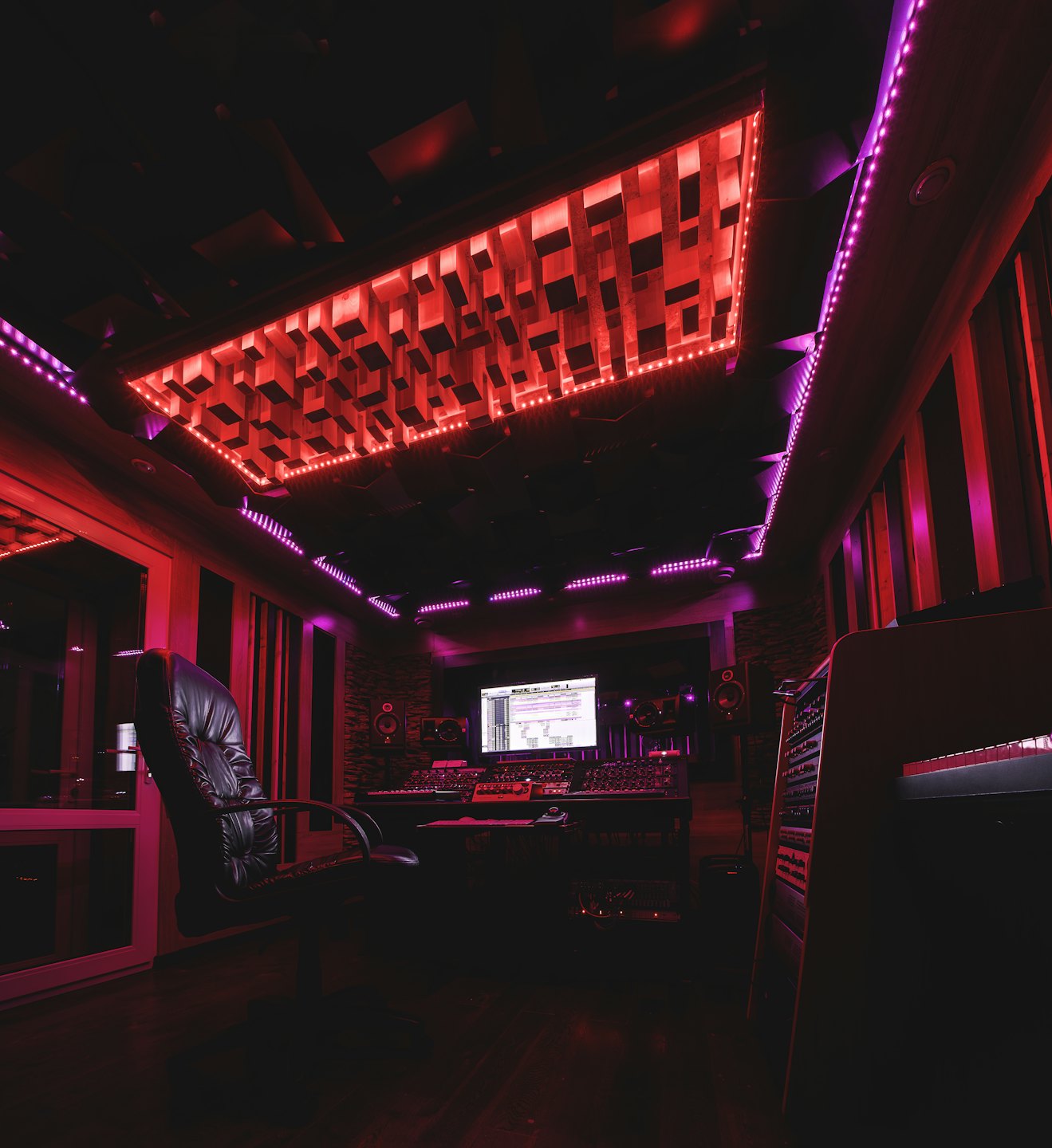 Empty music studio with sound equipment lit by red and purple lights.
