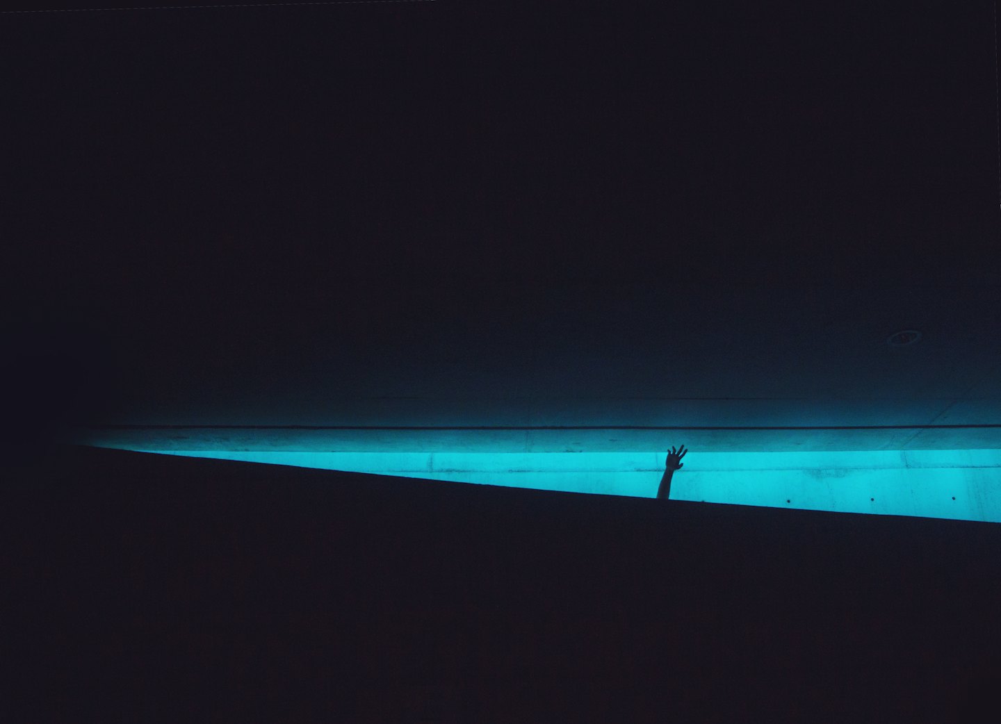 Silhouette of a hand reaching up through cyan light.